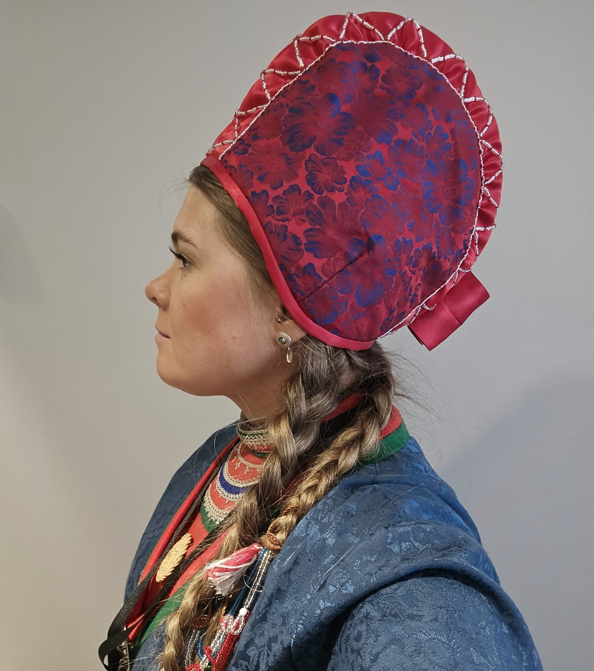 Tanja Nordfjäll i profil klädd i traditionella samiska kläder och en röd mönstrad huvudbonad.