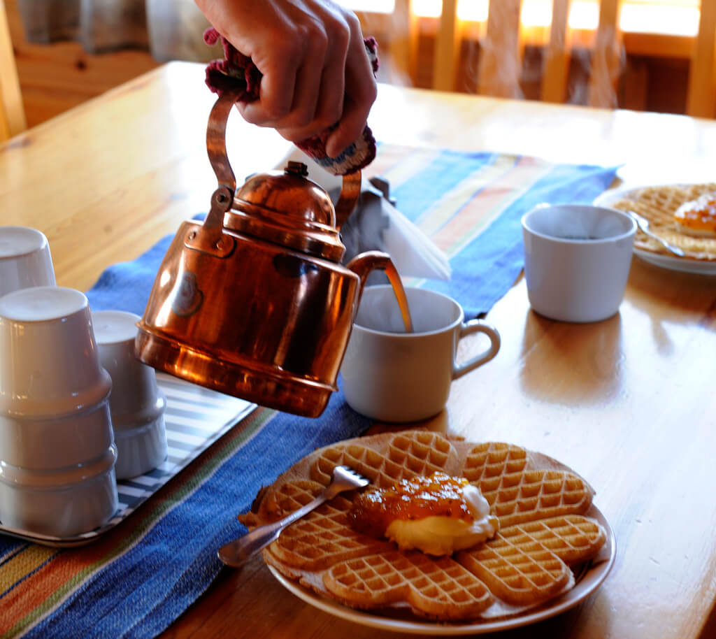Kaffe serveras ur kopparkanna till våfflor med sylt och grädde